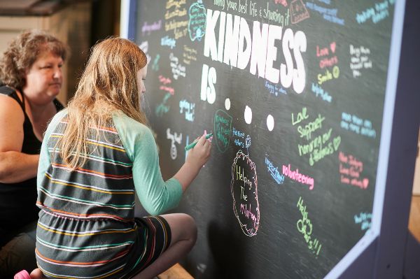 Women at a chalkboard writing in a message about kindness